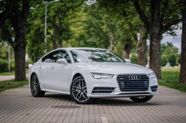 Valmiera, Letonya - 1 Ağustos 2024 - Beyaz bir Audi sedan ağaçlık bir caddeye park edilmiş, arka planda gün ışığında yeşillik var..