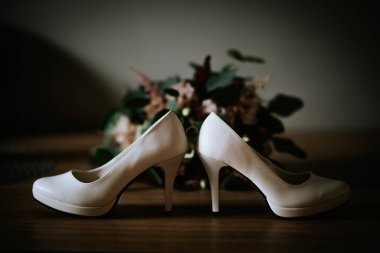 Cesis, Letonya - 12 Temmuz 2024 - Aralarına dengelenmiş bir alyans ile arka arkaya yerleştirilmiş iki yüksek topuklu ayakkabı, bulanık çiçekli bir arka planda..