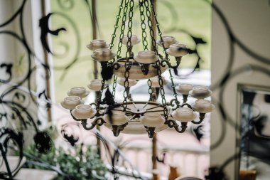 Cesis, Letonya - 12 Temmuz 2024 - Tavandan sarkan, dekoratif işlenmiş demirden desenlere bakan mum şekilli bir avize.