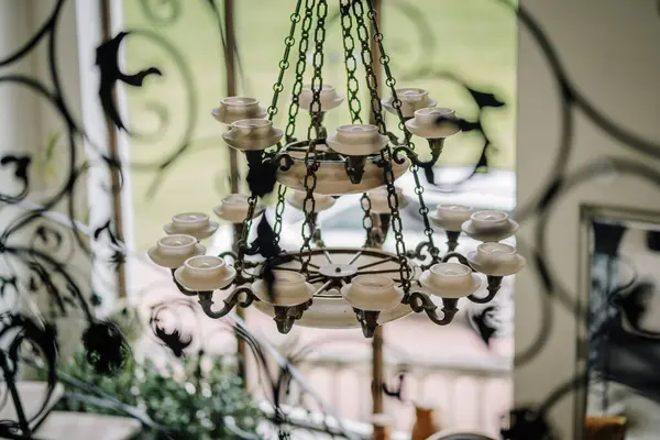 Cesis, Letonya - 12 Temmuz 2024 - Tavandan sarkan, dekoratif işlenmiş demirden desenlere bakan mum şekilli bir avize.