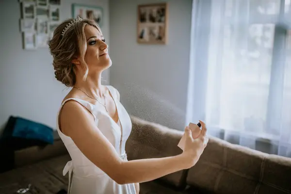 stock image Cesis, Latvia - July 12, 2024 - A bride in a white dress applies perfume, with a serene expression and her hair styled elegantly with a tiara.