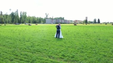 Gelin ve damat, arka planda saman balyaları ve binalarla yeşil bir arazide kucaklaşıp kırsal ve kentsel unsurların bir karışımını yakalıyor..