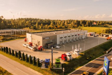 Valmiera, Letonya - 8 Ağustos 2024 - Sıcak bir günbatımı altında etrafı kamyonlar, arabalar ve yemyeşil yemliklerle çevrili bir İskandinav kamyon servis merkezinin havadan görünüşü.