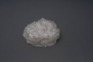 Gri bir zemin üzerinde ince, beyaz fiberglas iplikçikler küçük bir yığın, malzeme hassas ve lifli dokuyu sergiliyor.