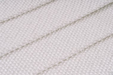 Görünür metal ipliklerle örülmüş beyaz dokuma kumaş, katlanmış kısımları ve karmaşık dokuyu gösteriyor. Resim dokuma desenini vurgular.