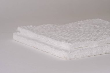 Düz beyaz bir zemin üzerinde dokulu, lifli bir yüzeye sahip beyaz fiberglas minderlerin yakın çekimi. Görüntü, materyalin kalınlığını ve dokusunu gösteriyor..
