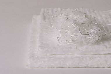 Üzerinde karmaşık fiberglas şeritler olan beyaz fiberglas paspaslar yakın plan, düz arkaplan üzerine kurulmuş. Görüntü materyalin dokusunu ve detaylarını gösterir..