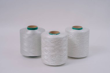 Three spools of white fiberglass yarn are arranged in a row on a neutral background, showcasing their texture and industrial design. clipart