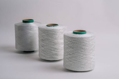 Arka arkaya dizilmiş üç adet beyaz fiberglas iplik makarası, temiz bir arka plan, farklı dokular ve kalınlıklar gösteriyor..