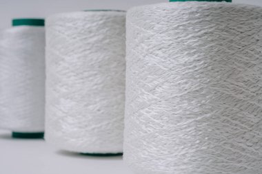 Üst üste dizilmiş üç adet beyaz fiberglas iplik makarasının yakın plan görüntüsü, beyaz arkaplana karşı dokularını ve dokuma şekillerini gösteriyor.