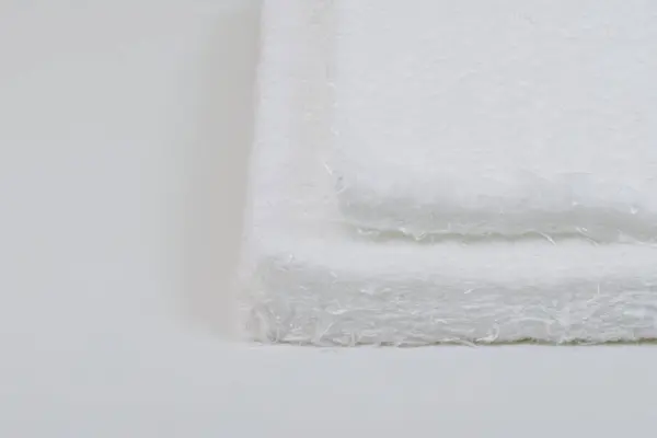 stock image Close-up of two stacked fiberglass mats with a fibrous texture on a white surface, highlighting their soft and fluffy appearance.