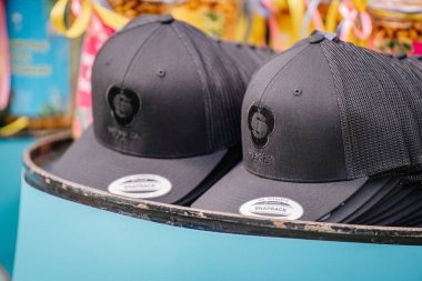 Valmiera, Letonya - 17 Ağustos 2024 - Yaz festivali. Valmiera Glass logosu olan siyah snapback kapaklar bir açık hava etkinliğinde düzgünce sergileniyor. Kapaklarda örgü sırtlar ve işlemeli logolar var..