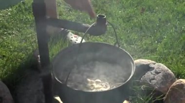 Bir insan, ahşap bir tahtadan kesilmiş eti, açık bir kamp ateşinin üzerinde buharlı bir tencereye koyar ve köy ortamında yemek hazırlar..