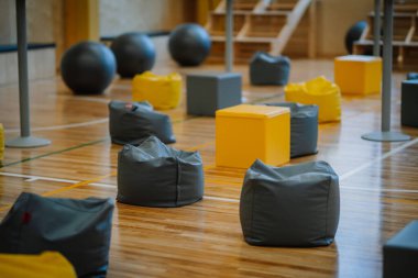 Valmiera, Letonya - 26 Nisan 2024 - Bir etkinlik ya da etkinlik için ayarlanmış gri ve sarı fasülye torbaları, fitness topları ve küp içeren bir spor salonu.