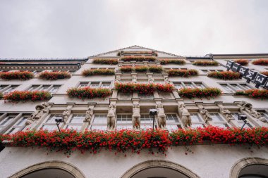 Münih, Almanya - 13 Eylül 2024 - Kırmızı çiçek kutuları ve heykellerle süslenmiş, detaylı mimari ve birden fazla pencerenin yer aldığı bir bina.