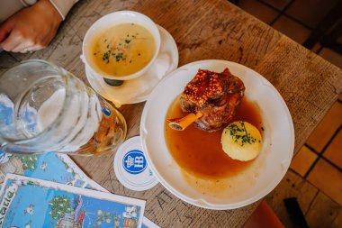 Münih, Almanya - 13 Eylül 2024 - Hofbrauhaus, Münih, Almanya 'da ahşap bir masada servis edilen geleneksel Bavyera yemeği, domuz budu, patates köftesi ve bira.