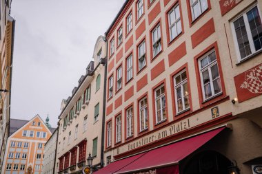 Münih, Almanya - 13 Eylül 2024 - Münih, Almanya 'da Augustiner am Platzl ön cephelerinde kırmızı tenteleri ve dekoratif mimarisi bulunan bir dizi renkli, tarihi bina.
