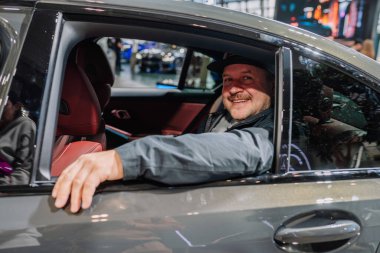 Münih, Almanya - 13 Eylül 2024 - Bir arabanın içinde oturan gülümseyen bir adam, elini kapıya dayamış pencereden dışarı bakıyor..