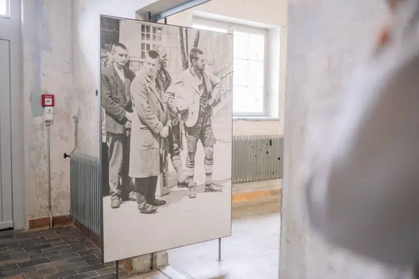 stock image Munich, Germany - September 13, 2024 - A historical black-and-white photo of a group of men, possibly prisoners or detainees, displayed in a museum exhibit room with vintage decor.