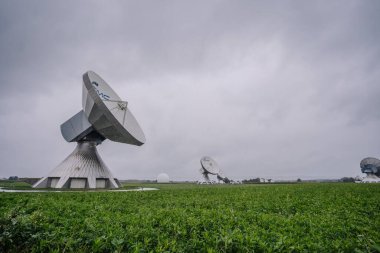 Raisting, Almanya - 14 Eylül 2024 - Geniş bir alanda uydu çanakları, bulutlu bir gökyüzü altındaki iletişim istasyonunun bir parçası, modern teknoloji ve tarımın sergilendiği.
