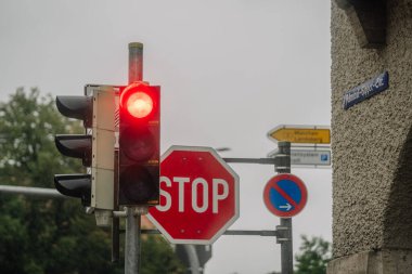 Bavyera, Almanya - 14 Eylül 2024 - Kırmızı ışığa yakın çekim, dur işareti, yağmurlu bir günde park yeri tabelası yok, arka planda sokak adı ve yön işareti var.