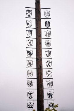 Bavaria, Germany - September 14, 2024 - A maypole adorned with various metal coat of arms symbols representing different trades or guilds, set against a misty gray sky. clipart