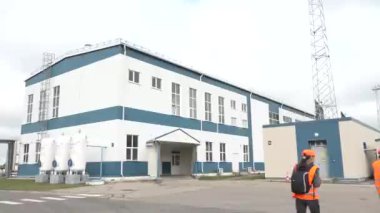 Sigulda, Letonya - 10 Ağustos 2024 - Dışarıda üç beyaz gaz tankı bulunan sanayi binası, güvenlik ekipmanları ve ön planda turuncu kasklı bir işçi.