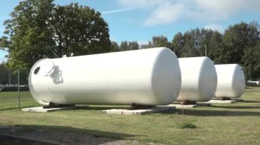 Sigulda, Letonya - 10 Ağustos 2024 - Üç büyük endüstriyel depolama tankı, ağaçlar ve açık bir gökyüzü ile çevrili, çimenli bir alana yerleştirilir..