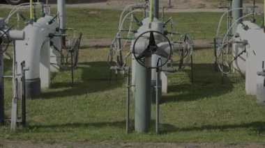 Sigulda, Letonya - 10 Ağustos 2024 - Çimenli bir alanda geniş kontrol vanaları ve bağlı borular gösteren açık hava endüstriyel tesisi.