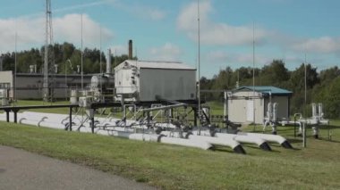 Sigulda, Letonya - 10 Ağustos 2024 - Beyaz boru hatları, küçük binaları ve mavi gökyüzünün altındaki çimenli bir alana kurulmuş metal bir geçidi olan açık hava sanayi tesisi.