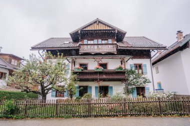 Bavyera, Almanya - 14 Eylül 2024 - Ahşap balkonları, çiçek açan çiçekleri ve yağmurlu bir günde yağmurlu bir köyde yakalanan çitli bir bahçesi olan büyüleyici bir Bavyera evi.