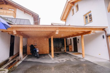 Bavaria, Germany - September 14, 2024 - A wooden carport attached to a modern house, sheltering a motorcycle on a rainy day. Firewood is stacked in the background. Copy space available. clipart