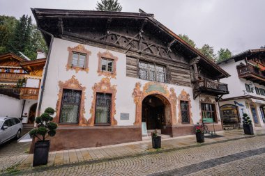 Bavyera, Almanya - 14 Eylül 2024 - Karmaşık duvar resimleri, ahşap balkon ve Avrupa 'da bir köyün kaldırım taşı sokağında kemerli bir kapı ile büyüleyici bir Bavyera tarzı ev.