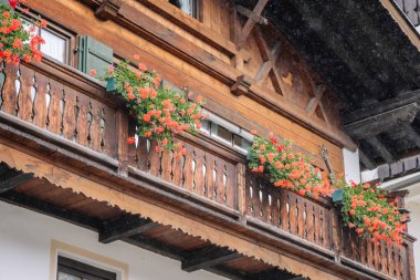 Bavyera, Almanya - 14 Eylül 2024 - Geleneksel bir Avrupa evinde canlı kırmızı çiçeklerle süslenmiş büyüleyici bir ahşap balkon. Karmaşık ahşap ve çiçek kutuları rahat bir atmosfer yaratıyor..