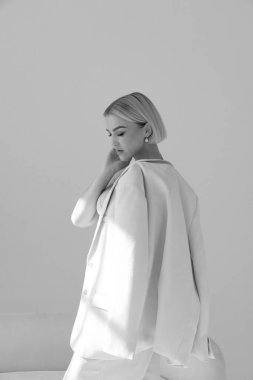 Pembe takım elbiseli zarif bir kadın, yumuşak doğal ışıkla omuzlarına montunu geçirmiş, düşünceli bir şekilde aşağıya bakıyor..