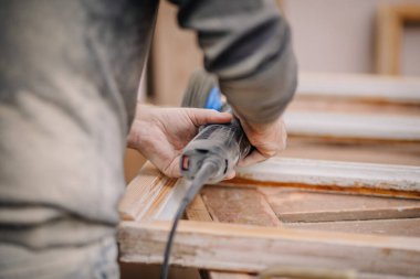 A close-up of a craftsman sanding a wooden frame using a power tool, focusing on the hands and tool during a woodworking project. clipart