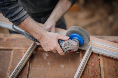 Tahta bir pencere çerçevesini pürüzsüz hale getirmek için zımpara makinesi kullanan bir adamın elleri. Resim araç ve manuel çalışmanın ayrıntılarını yakalar