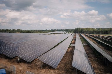 Ağaçlarla çevrili bulutlu bir gökyüzünün altında sıralanmış geniş bir güneş çiftliği..