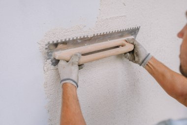 Bir işçi duvardaki alçıyı çentik şeklinde bir malayla düzleştirir, düz bir bitiş üzerine odaklanır. İnşaat çalışmalarına yakın çekim.