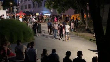 Valmiera, Letonya - 23 Temmuz 2024 - Sokak lambalarıyla aydınlatılmış, yemek tezgahları ve canlı bir atmosferle sosyalleşen ve yürüyen bir grup insan.