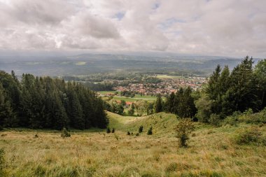 Bavyera, Almanya - 15 Eylül 2024 - Yoğun ormanlar, yuvarlanan tepeler ve bulutlu bir gökyüzünün altındaki açık arazilerle çevrili bir Bavyera köyünün panoramik görüntüsü.