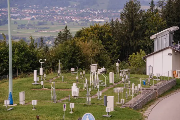 stock image Bavaria, Germany - September 15, 2024 - A weather station in Bavaria with various meteorological instruments on a grassy field, with a village and hills in the background.