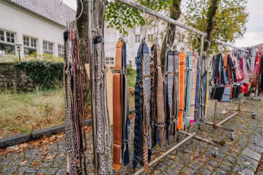 Bavyera, Almanya - 15 Eylül 2024 - Arka planda kaldırım taşları ve ağaçların bulunduğu Bavyera 'daki bir markette askıda renkli desenli çanta askıları.