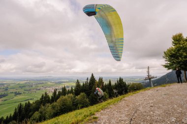 Bavyera, Almanya - 15 Eylül 2024 - Bavyera 'daki bir tepeden yeşil tarlalar, ormanlar ve aşağıdaki bulutlu gökyüzünün altındaki köylerle çevrili bir paraglider fırlatılıyor..