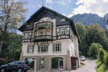 Bavyera, Almanya - 15 Eylül 2024 - Güneşli bir günde dağlık bir zemin üzerine kurulmuş yeşil panjurlu ve balkonlu geleneksel bir Bavyera evi.