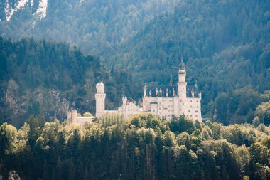 Bavyera, Almanya - 15 Eylül 2024 - Neuschwanstein Şatosu, arka planda dağlık bir arazi olan Bavyera 'nın ortasında görkemli bir şekilde duruyor..