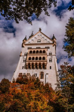 Bavyera, Almanya - 15 Eylül 2024 - Arkaplanda bulutlu bir gökyüzünün altında sonbahar ağaçları ve manzaralı bir vadi bulunan Neuschwanstein Kaleleri 'nin yakın görüntüsü
