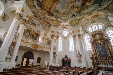 Bavyera, Almanya - 15 Eylül 2024 - Süslü sütunları, tavanda detaylı resimleri, vitray pencereleri ve ustalıkla oyulmuş sunağı olan büyük bir barok kilise iç mimarisi.