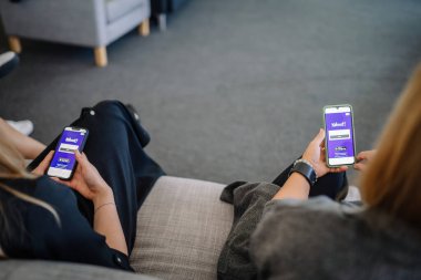 Riga, Letonya - 19 Eylül 2024 - Kanepede oturan iki kadın, ikisi de akıllı telefon kullanıyor, ekranlarında Kahoot uygulaması var,.