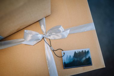 Riga, Latvia - September 19, 2024 - Close-up of a gift box wrapped with light blue ribbon and a forest-themed tag attached, ready for a special occasion. clipart